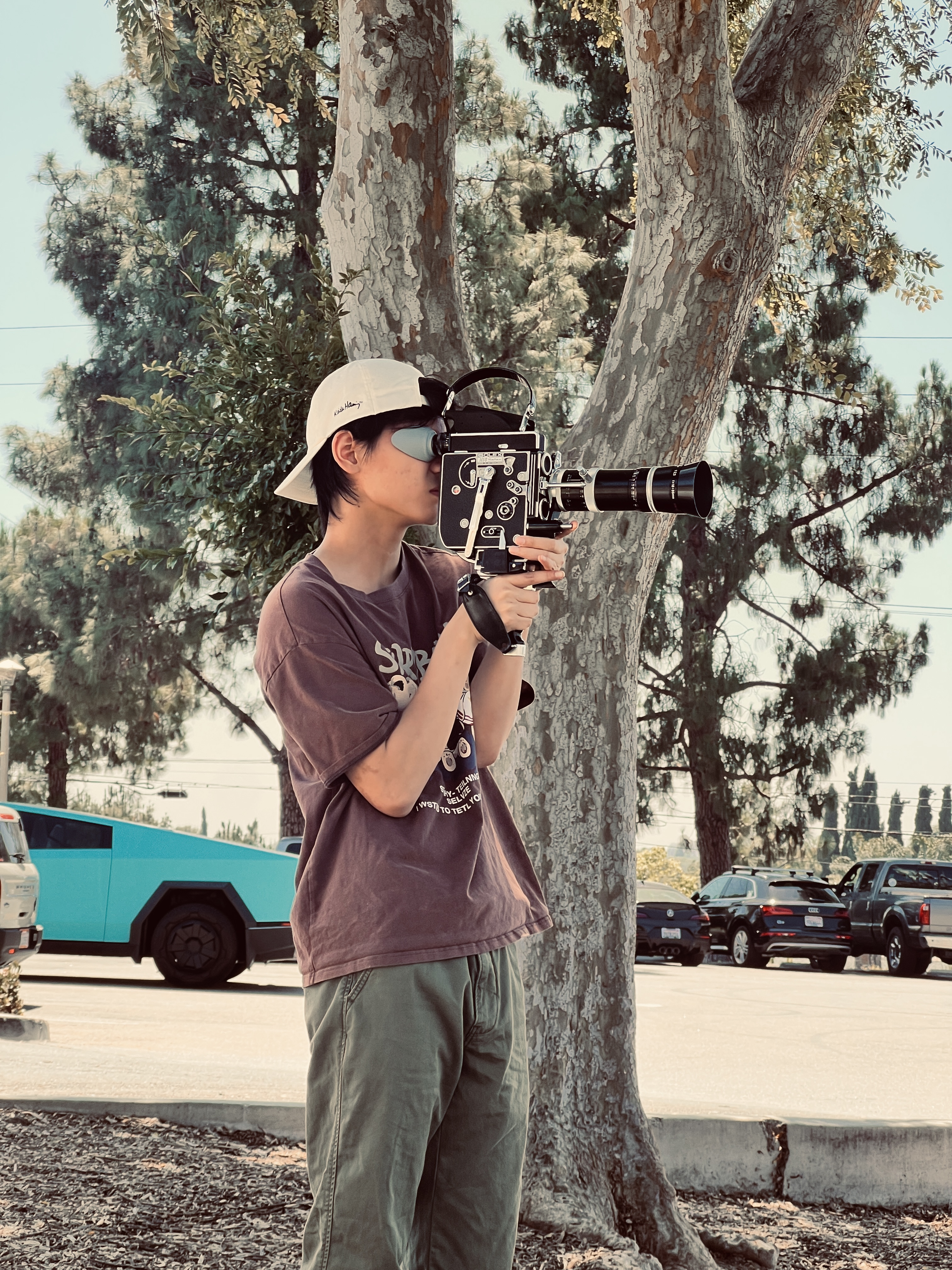 A filmmaker holding a movie camera outdoors beside a tree